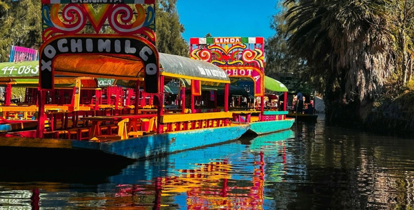 A colorful boat floating down a river next to a forest